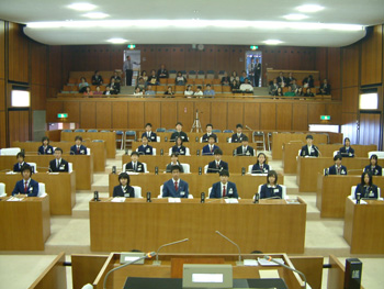 本会議場の議員席に着いた中学生の写真